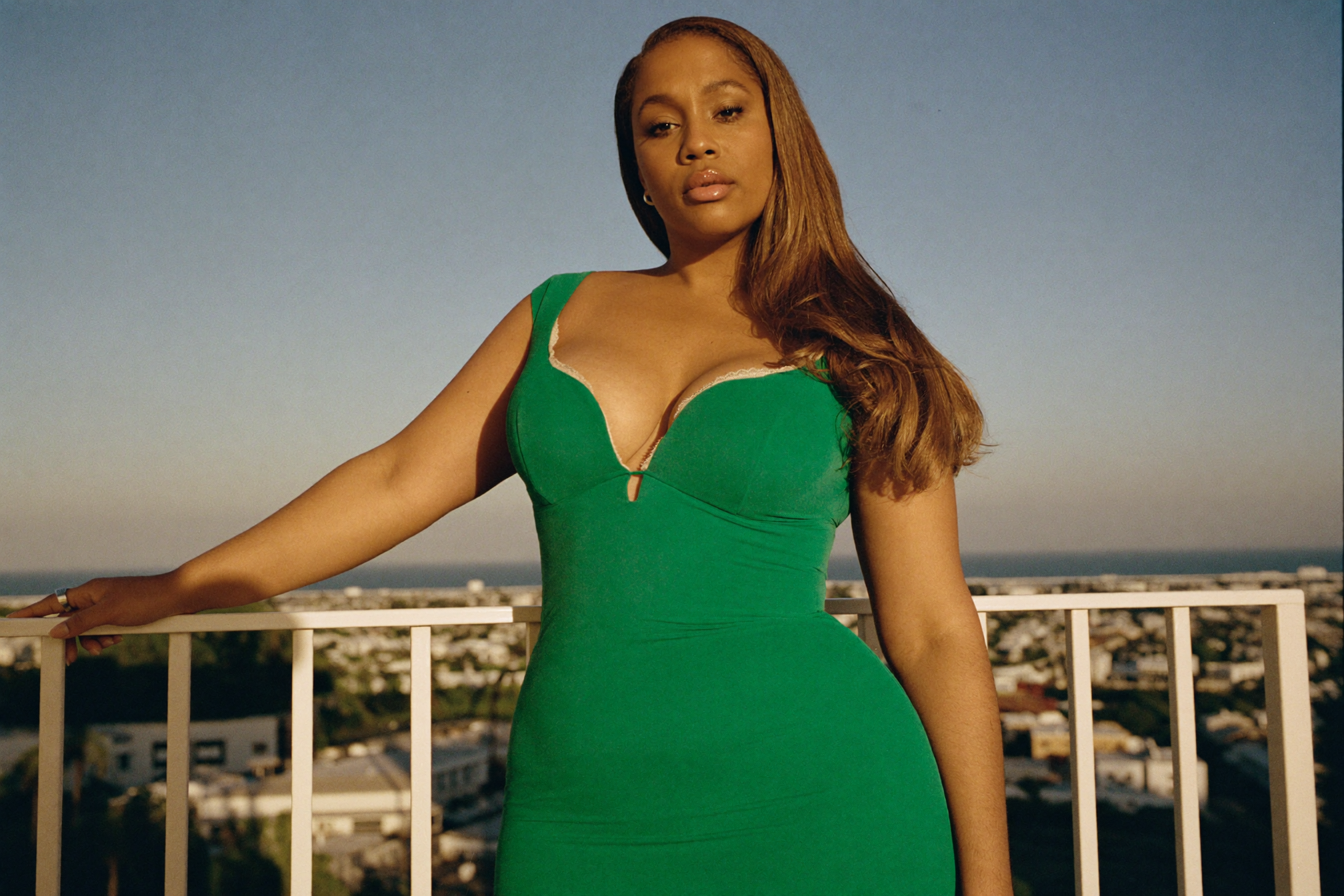 Confident curvy woman in a fitted emerald wrap dress on a balcony